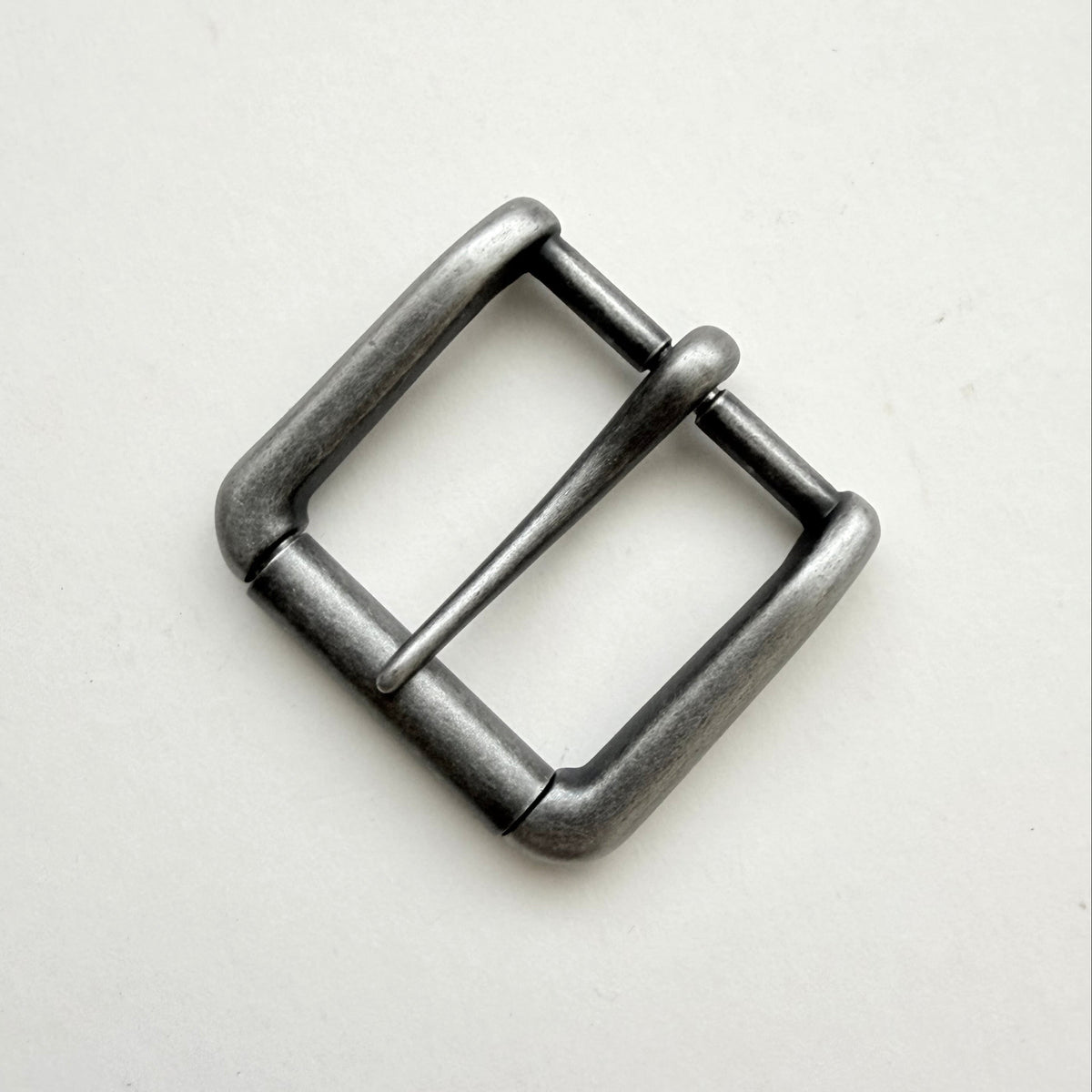 A single metal belt buckle with a square frame and single prong, finished in a dark gunmetal gray or antique silver tone, photographed on a plain off-white background.
