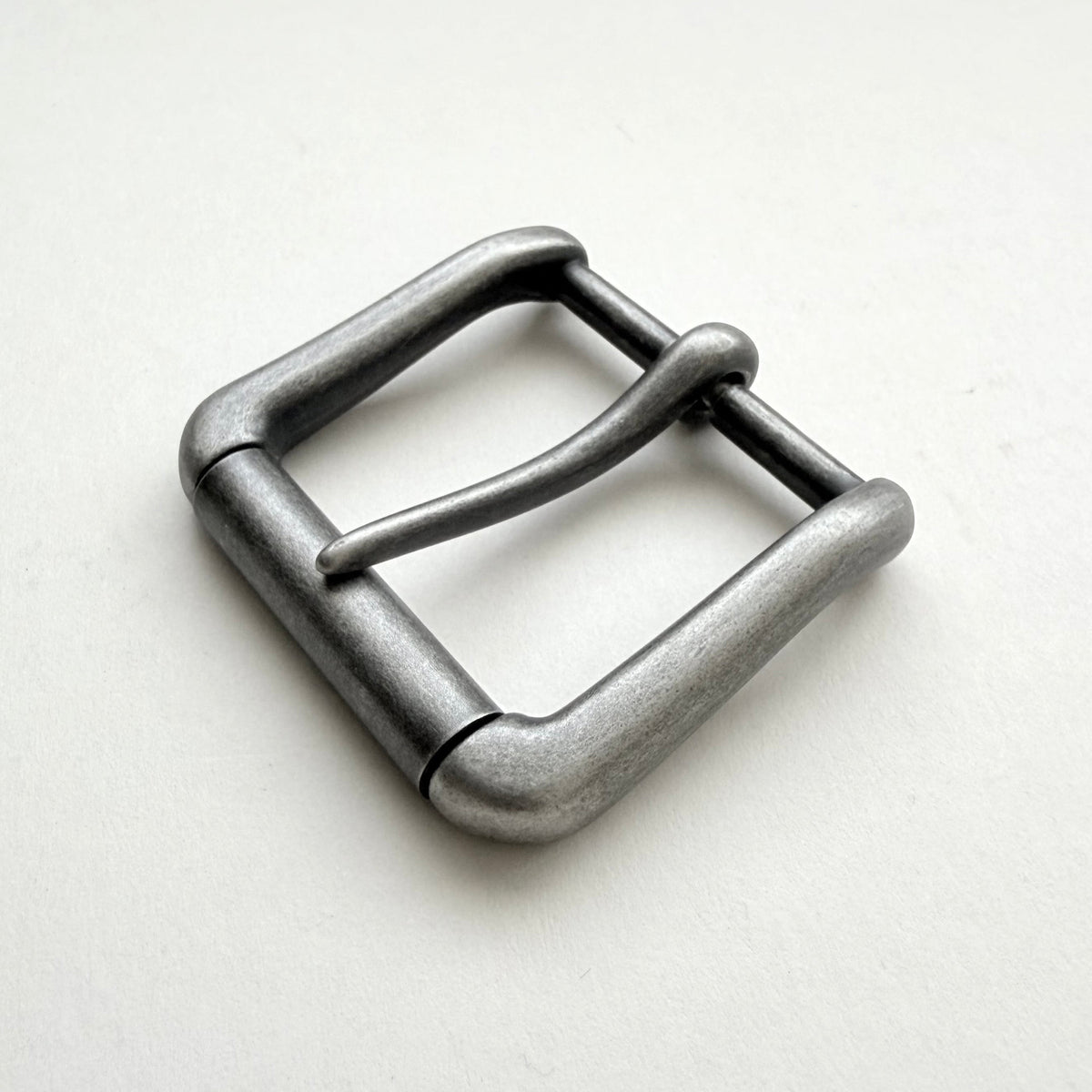 A single metal belt buckle with a rounded rectangular shape and a single prong, finished in a textured matte gray metal, shown on a plain off-white background.