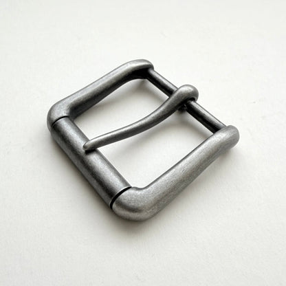 A single metal belt buckle with a rounded rectangular shape and a single prong, finished in a textured matte gray metal, shown on a plain off-white background.
