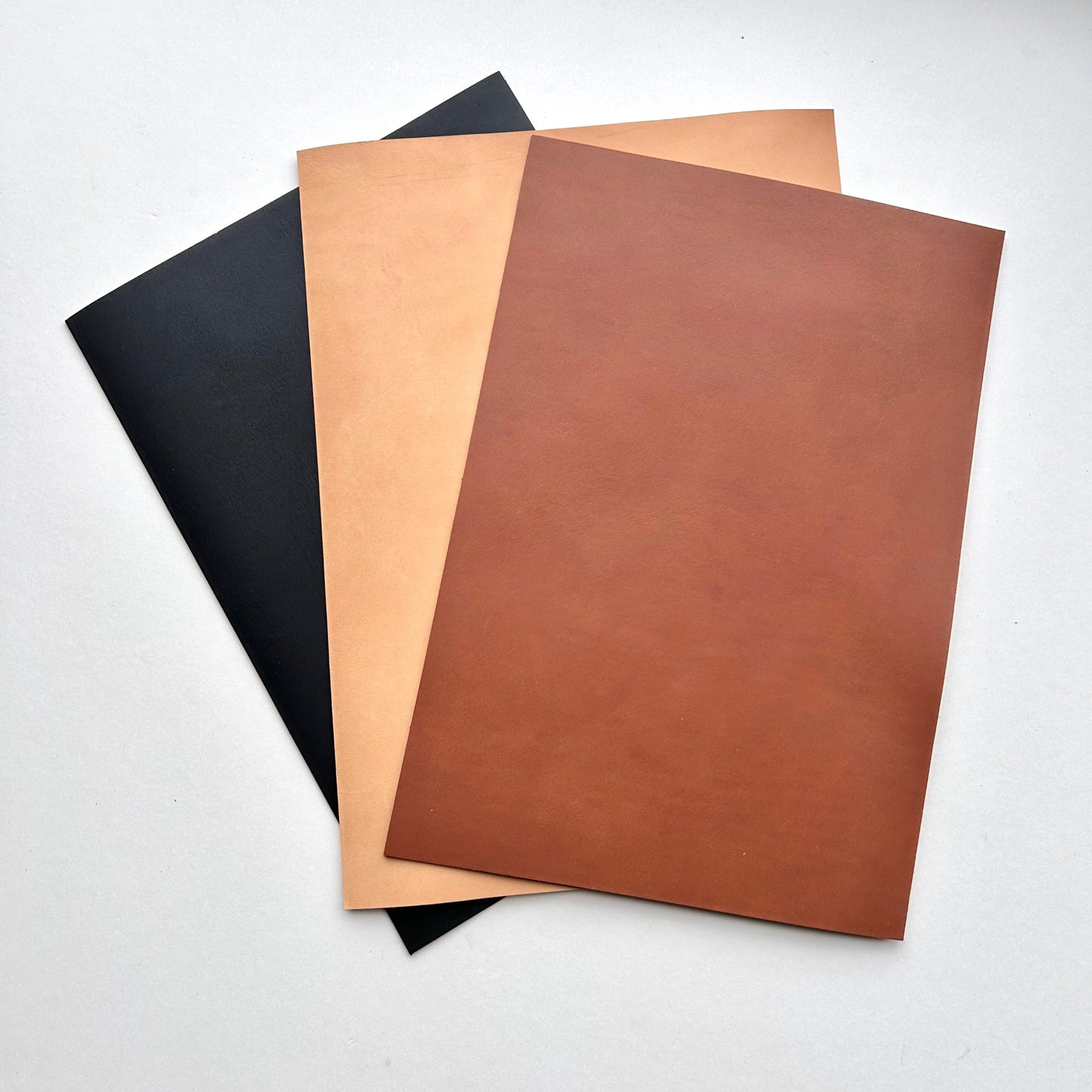 Three sheets of leather with black, brown, and beige colors on a white background