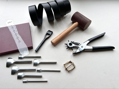 Collection of leathercraft tools including rotary punch, hammers, and metal components on a white surface.