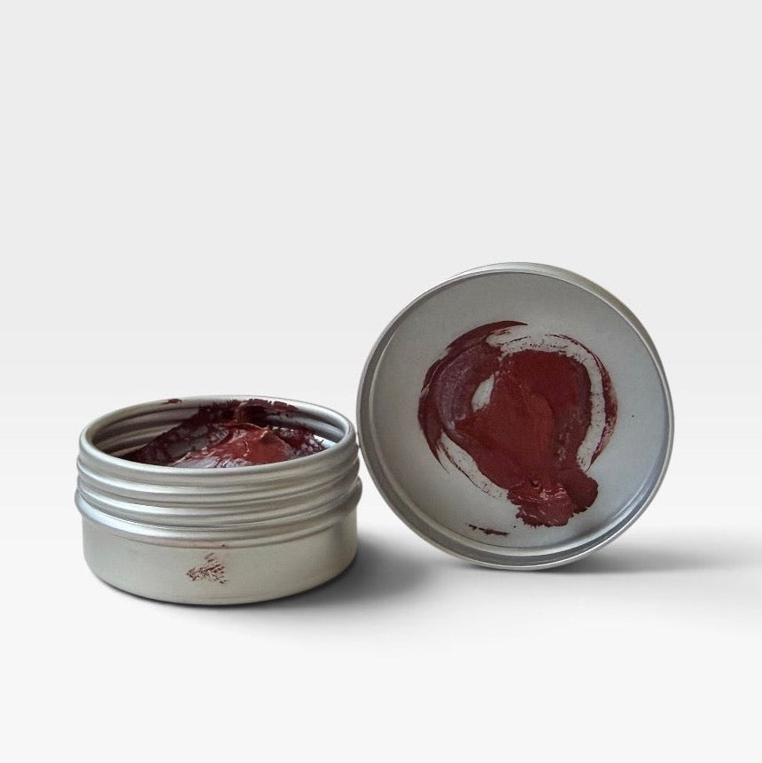 A small round silver metal tin of Bolpol Jewellers rouge with its lid off, showing a dark red balm or cream inside, photographed on a clean light grey background.