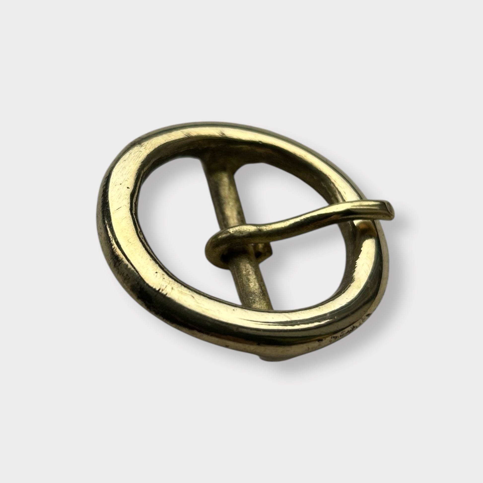 Gold coloured circular brass belt buckle on a light grey background, centre bar style.
