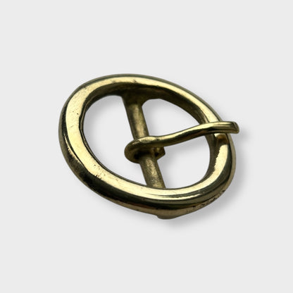 Gold coloured circular brass belt buckle on a light grey background, centre bar style.
