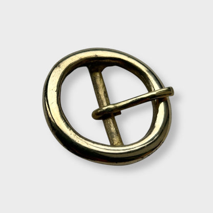 Gold coloured circular brass belt buckle on a light grey background, centre bar style.