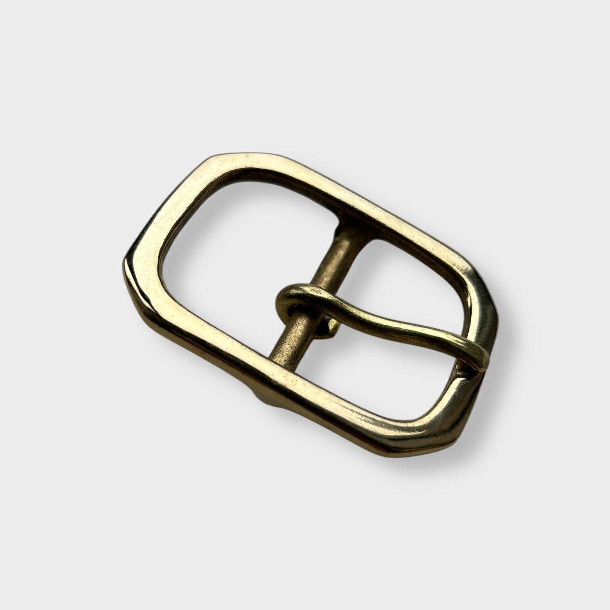 Gold coloured brass metal buckle with a centre bar on a light grey background.