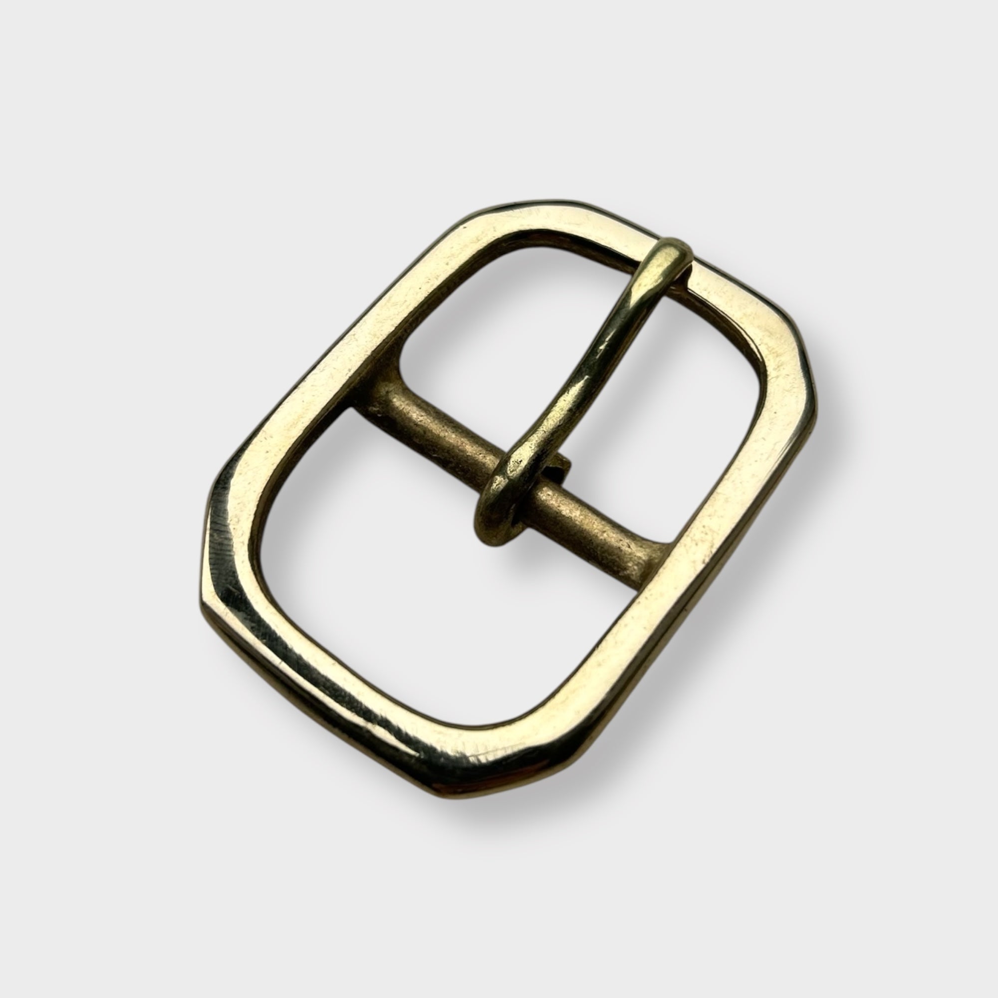 Gold coloured brass metal buckle with a centre bar on a light grey background.