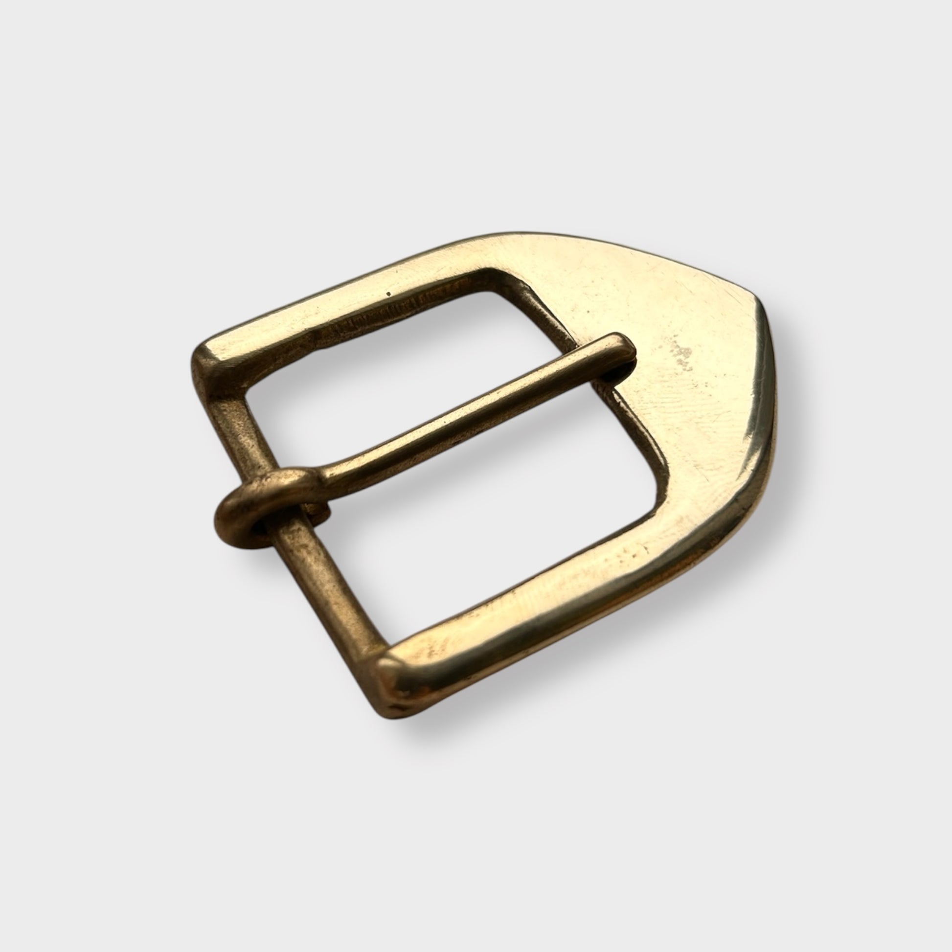 Gold coloured brass metal buckle on a light grey background.