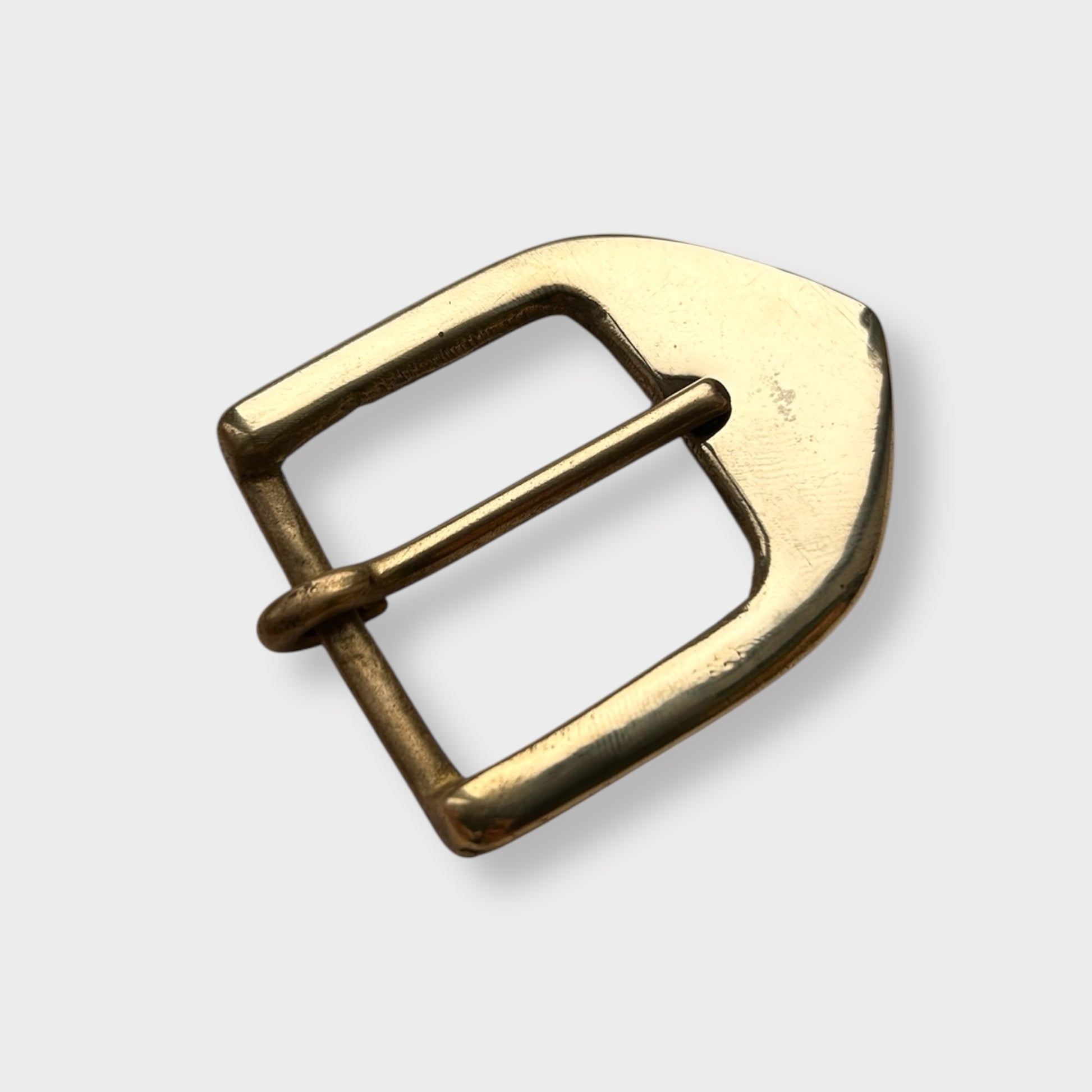 Gold coloured brass metal buckle on a light grey background.