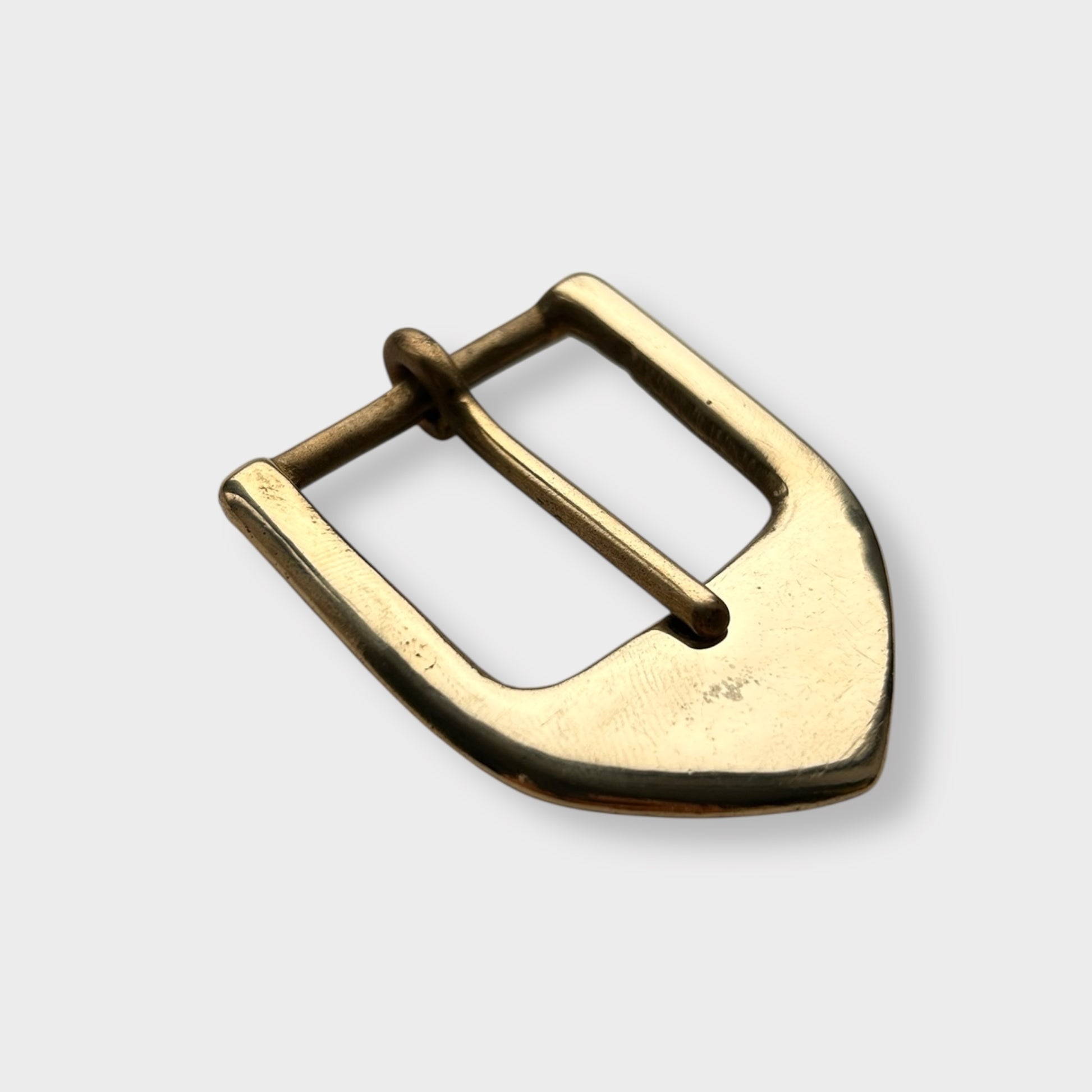 Gold coloured brass metal buckle on a light grey background.