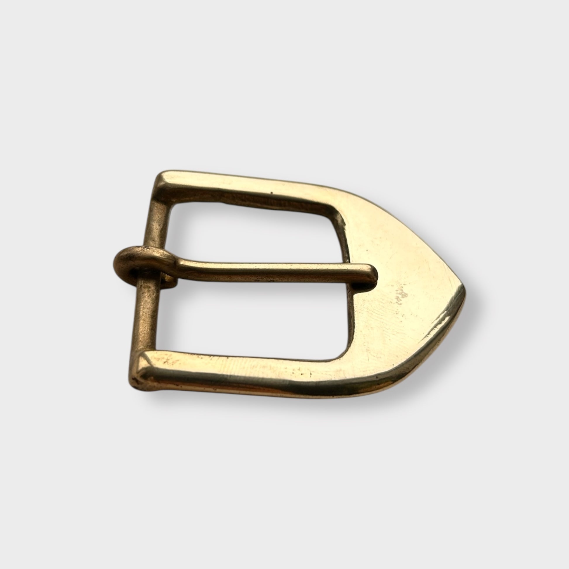 Gold coloured brass metal buckle on a light grey background.