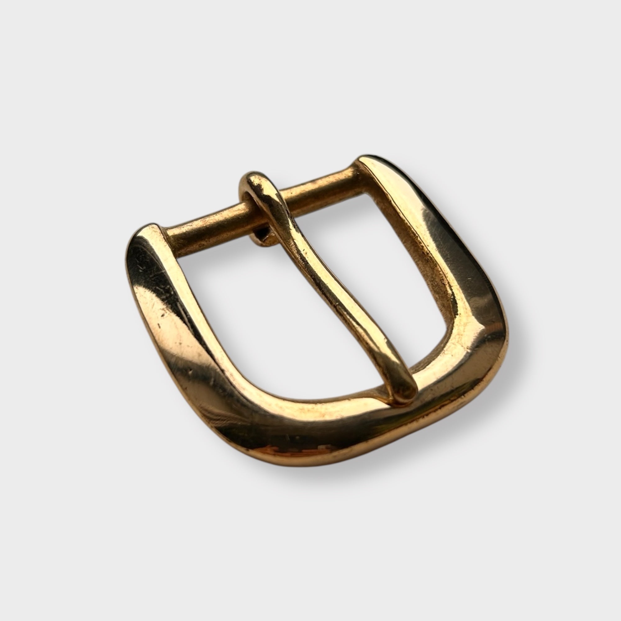Gold coloured brass metal buckle on a light grey background.