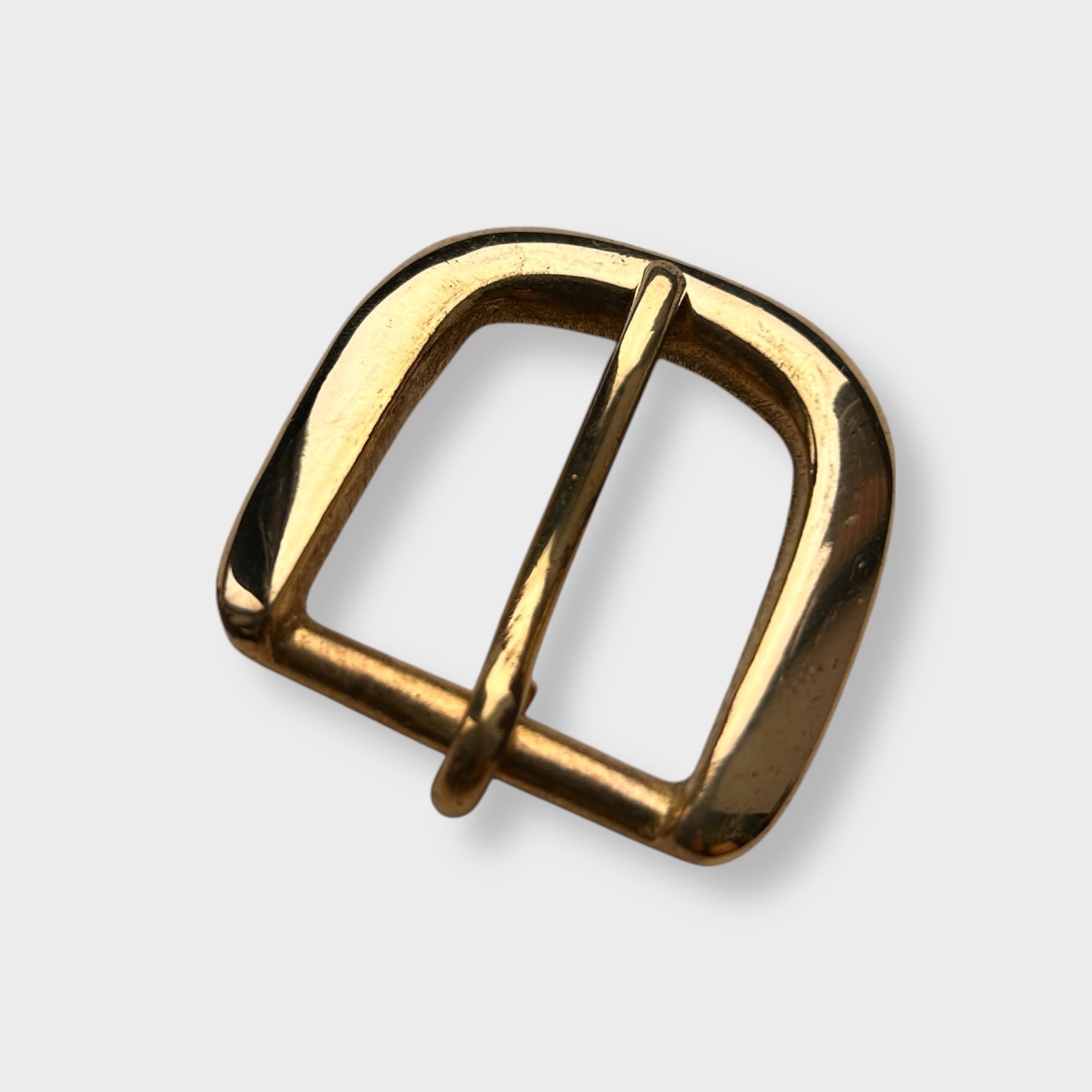 Gold coloured brass metal buckle on a light grey background.