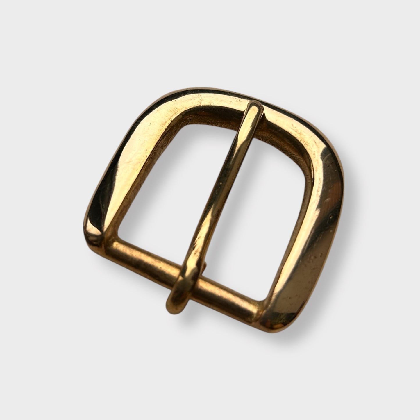 Gold coloured brass metal buckle on a light grey background.