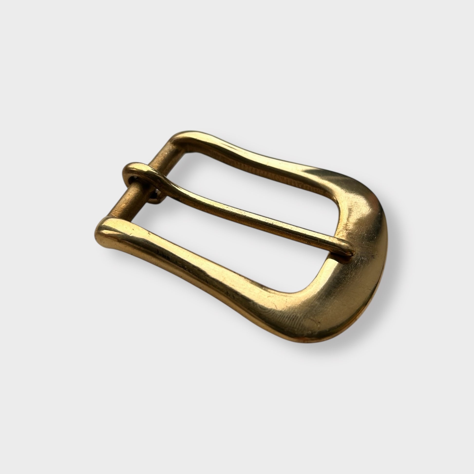 Gold coloured brass metal buckle on a light grey background.