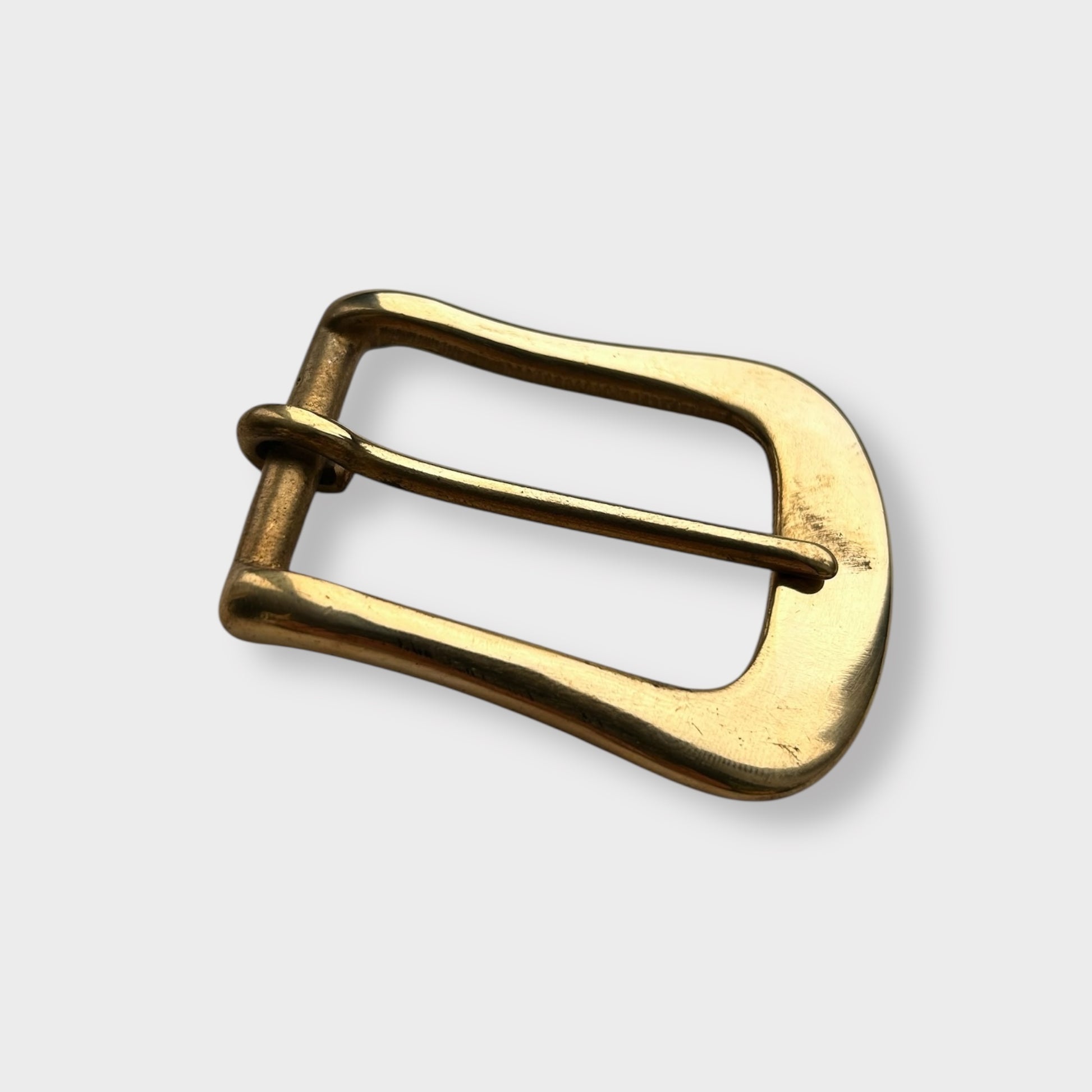 Gold coloured brass metal buckle on a light grey background.