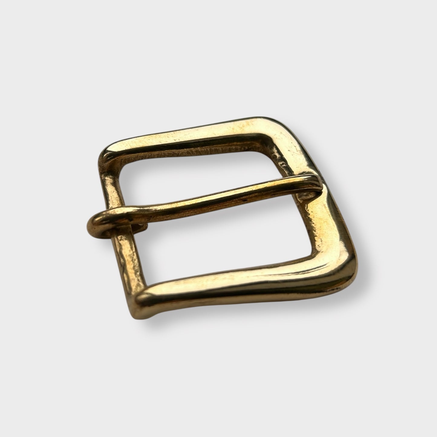 Gold coloured brass metal buckle on a light grey background.