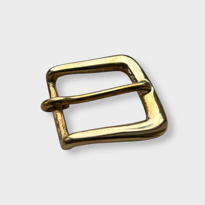 Gold coloured brass metal buckle on a light grey background.