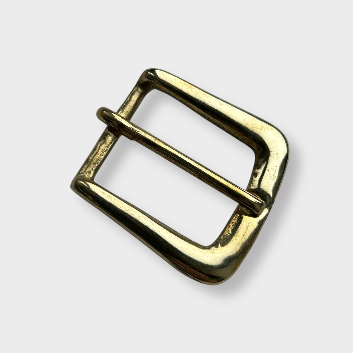 Gold coloured brass metal buckle on a light grey background.