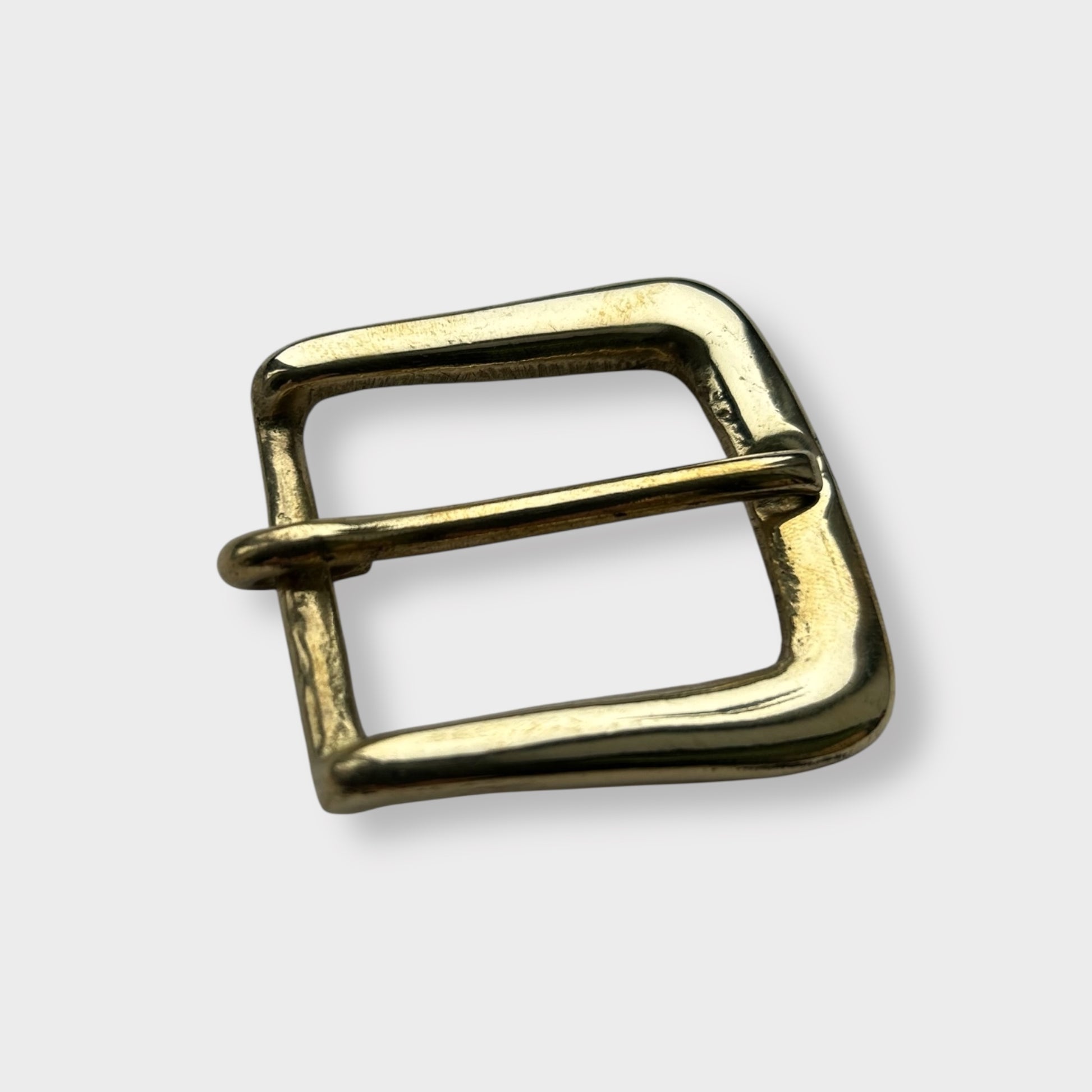 Gold coloured brass metal buckle on a light grey background.