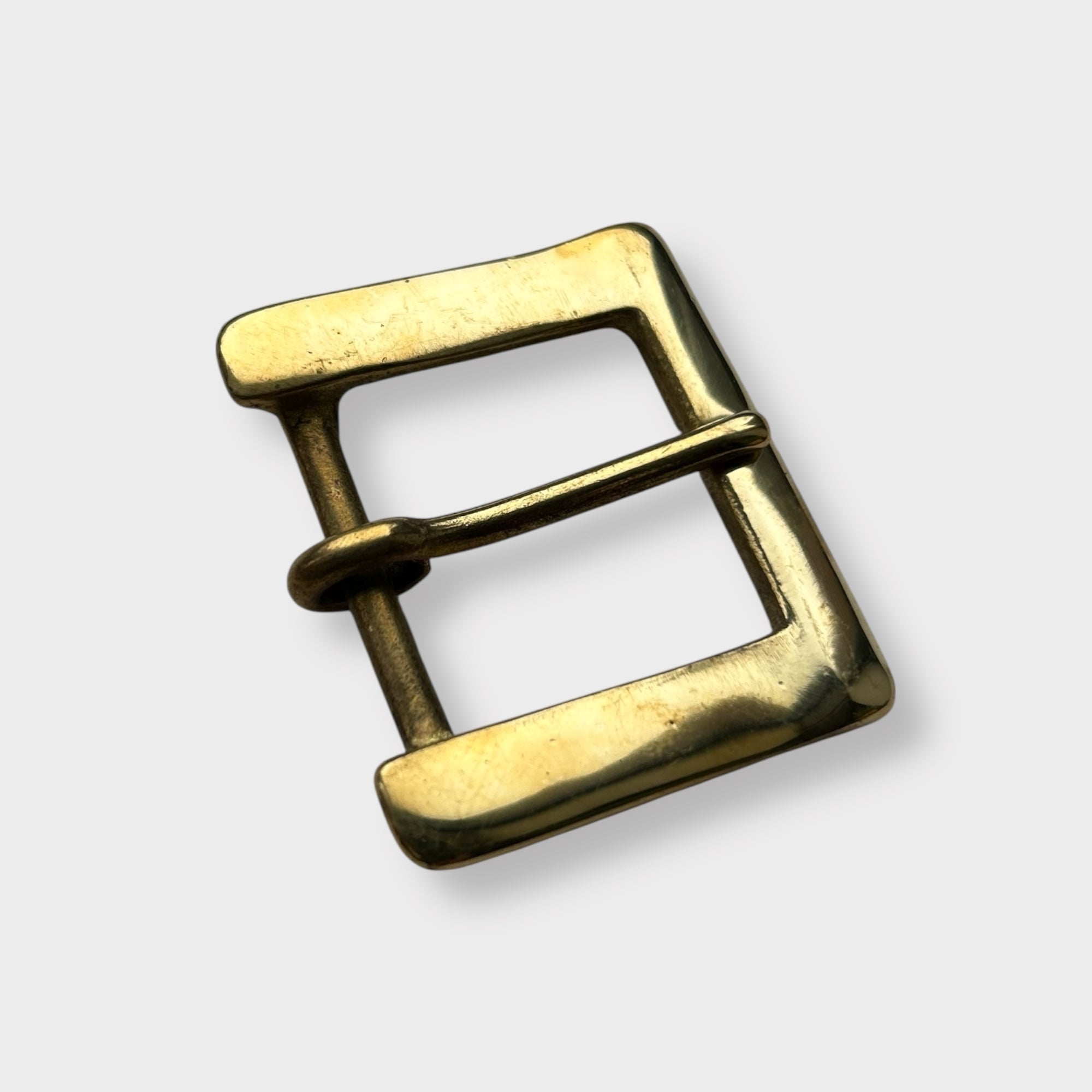 Gold coloured brass metal buckle on a light grey background.