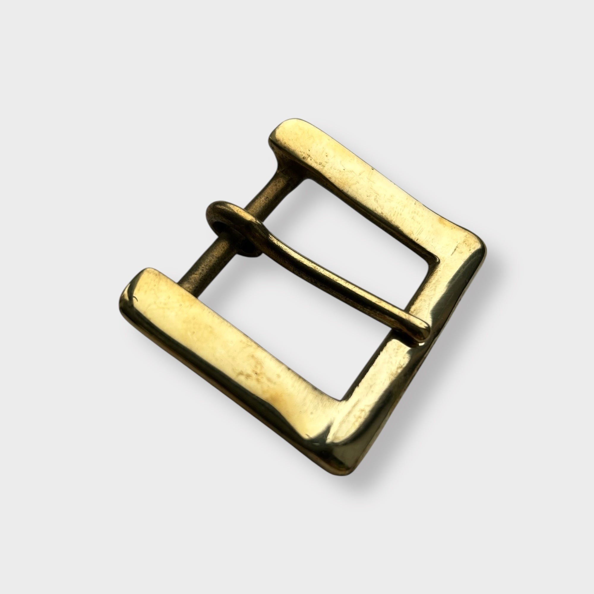 Gold coloured brass metal buckle on a light grey background.