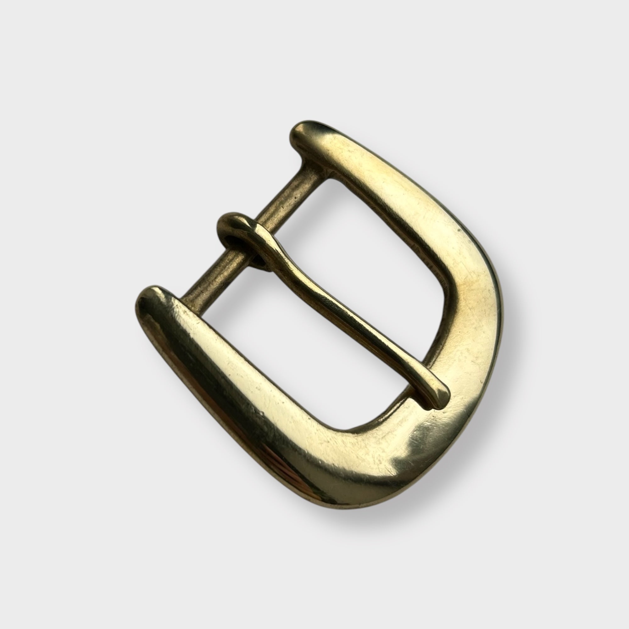 Gold coloured brass metal buckle on a light grey background.