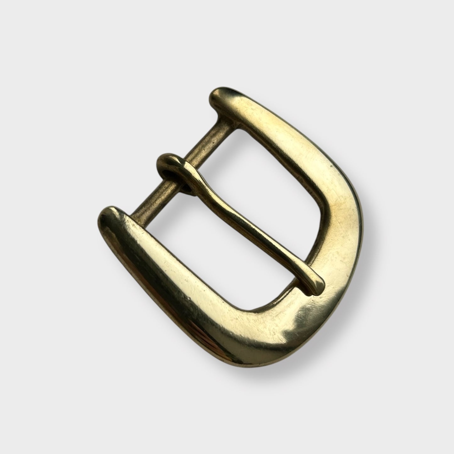 Gold coloured brass metal buckle on a light grey background.