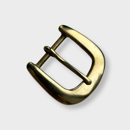 Gold coloured brass metal buckle on a light grey background.