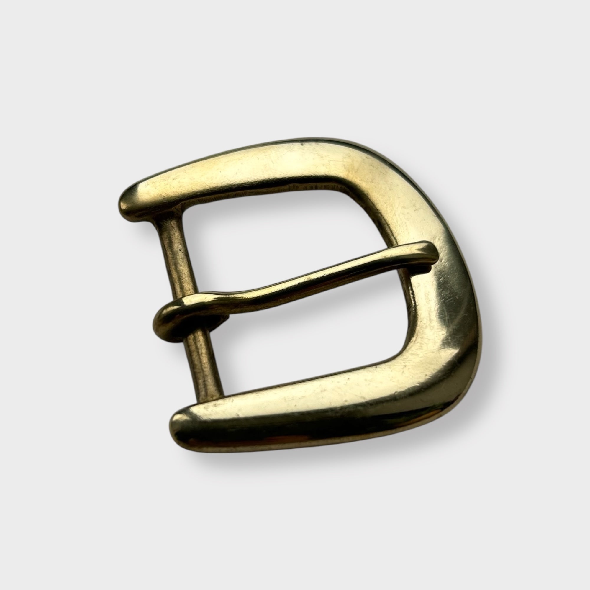 Gold coloured brass metal buckle on a light grey background.