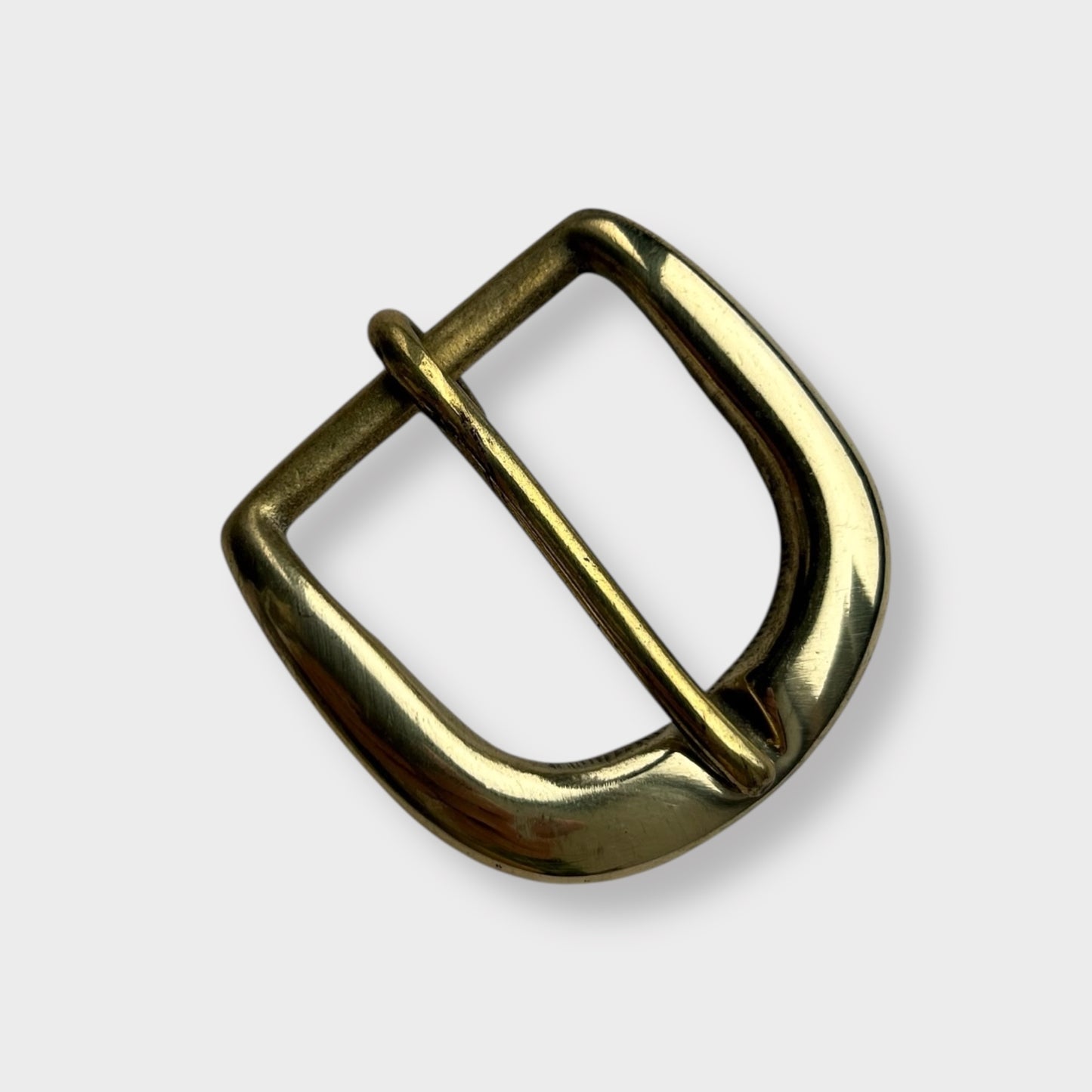 Gold coloured brass metal buckle on a light grey background.