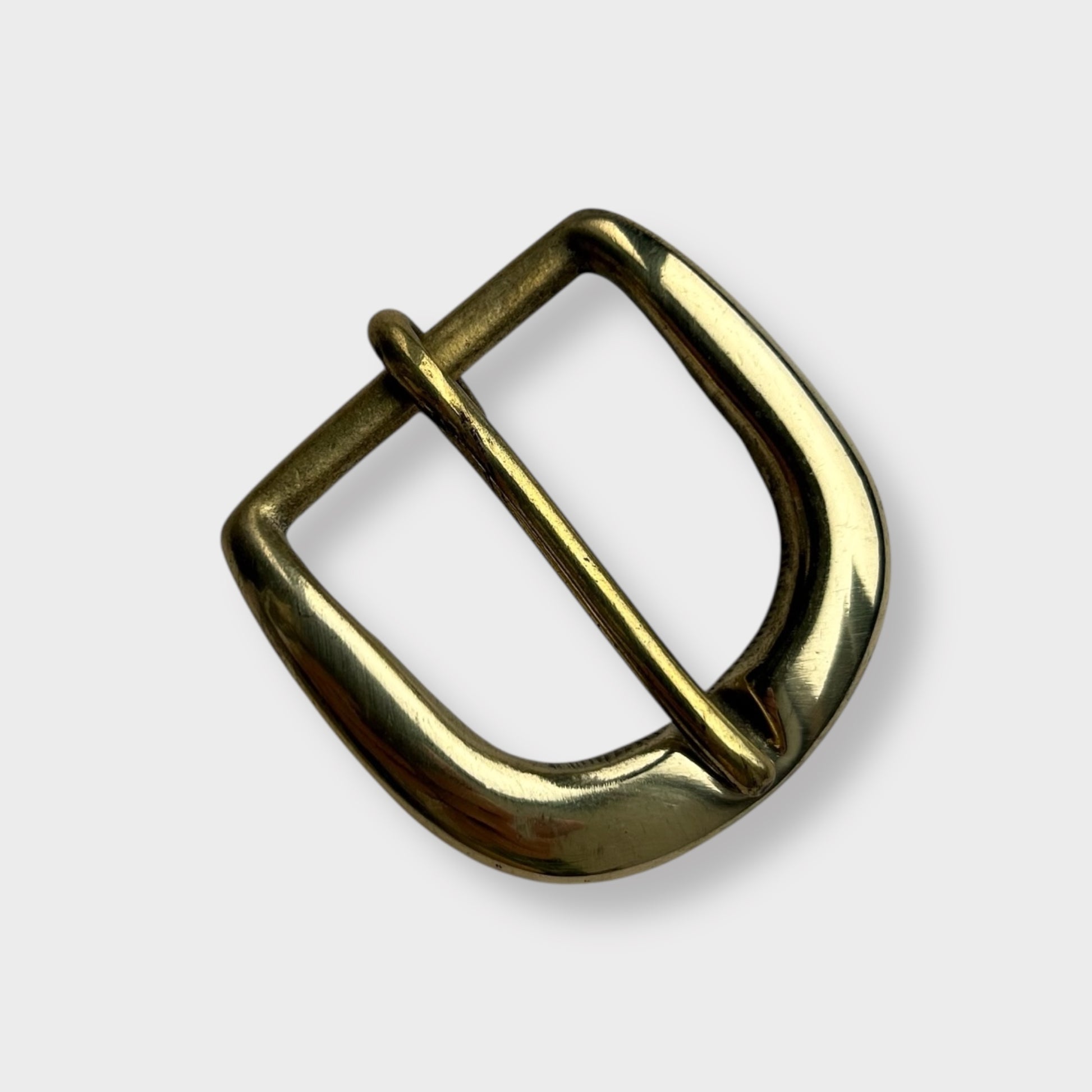 Gold coloured brass metal buckle on a light grey background.