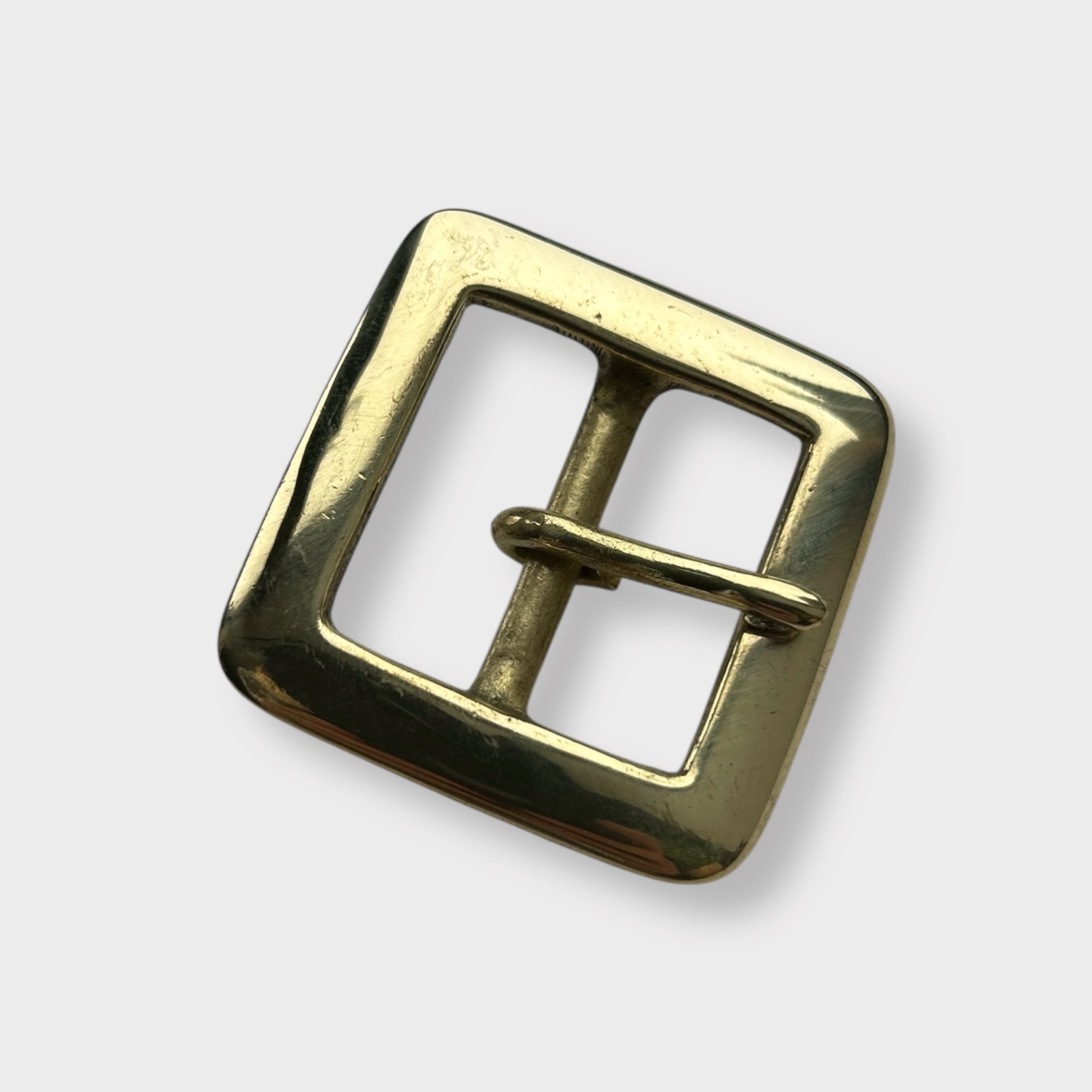 Gold coloured brass metal buckle on a light grey background.