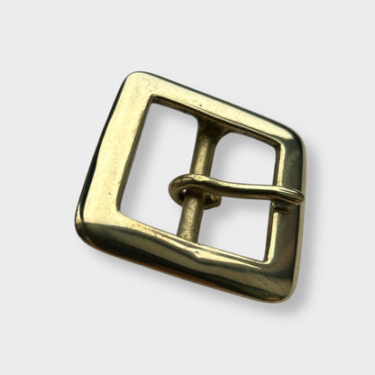 Gold coloured brass metal buckle on a light grey background.