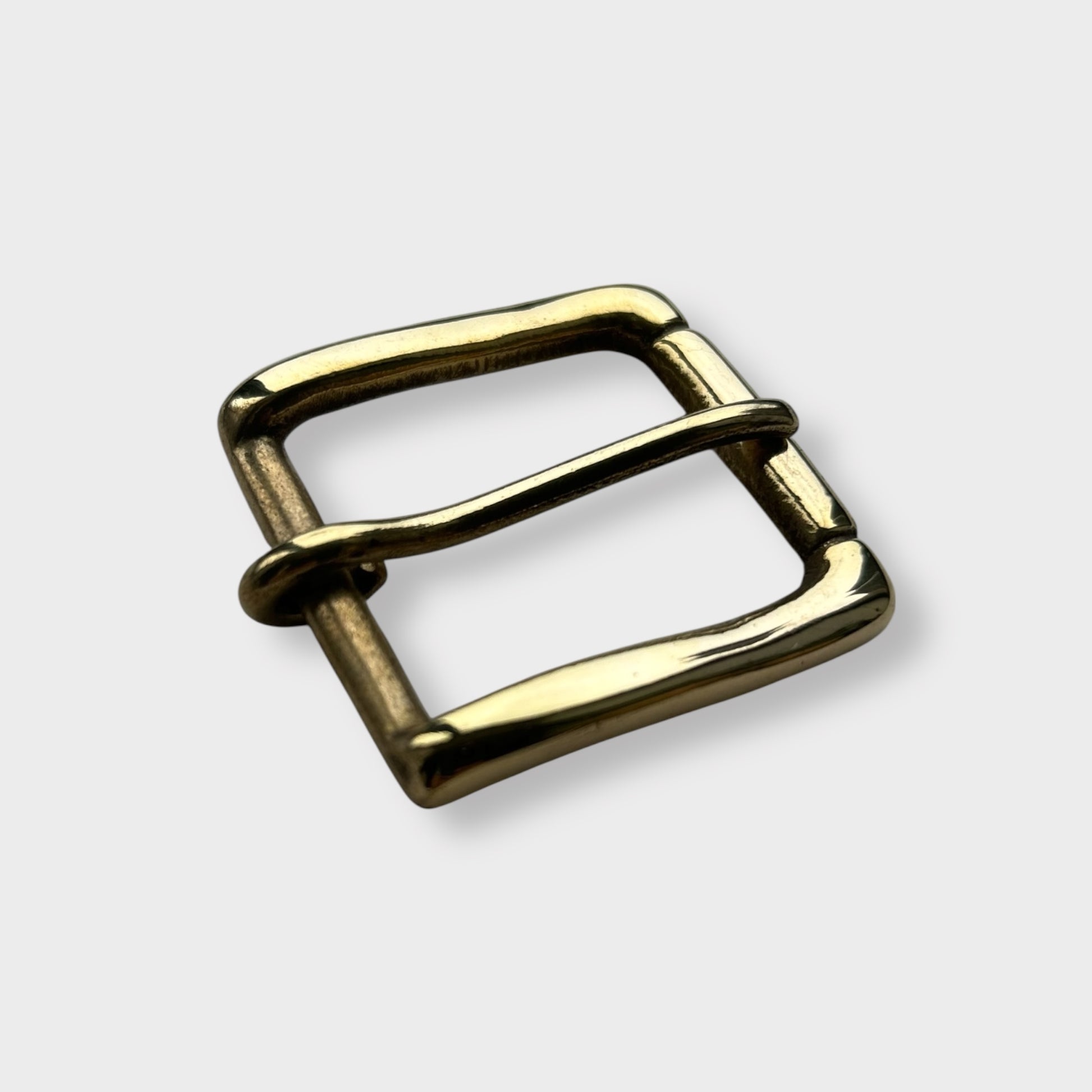 Gold coloured brass metal buckle on a light grey background.