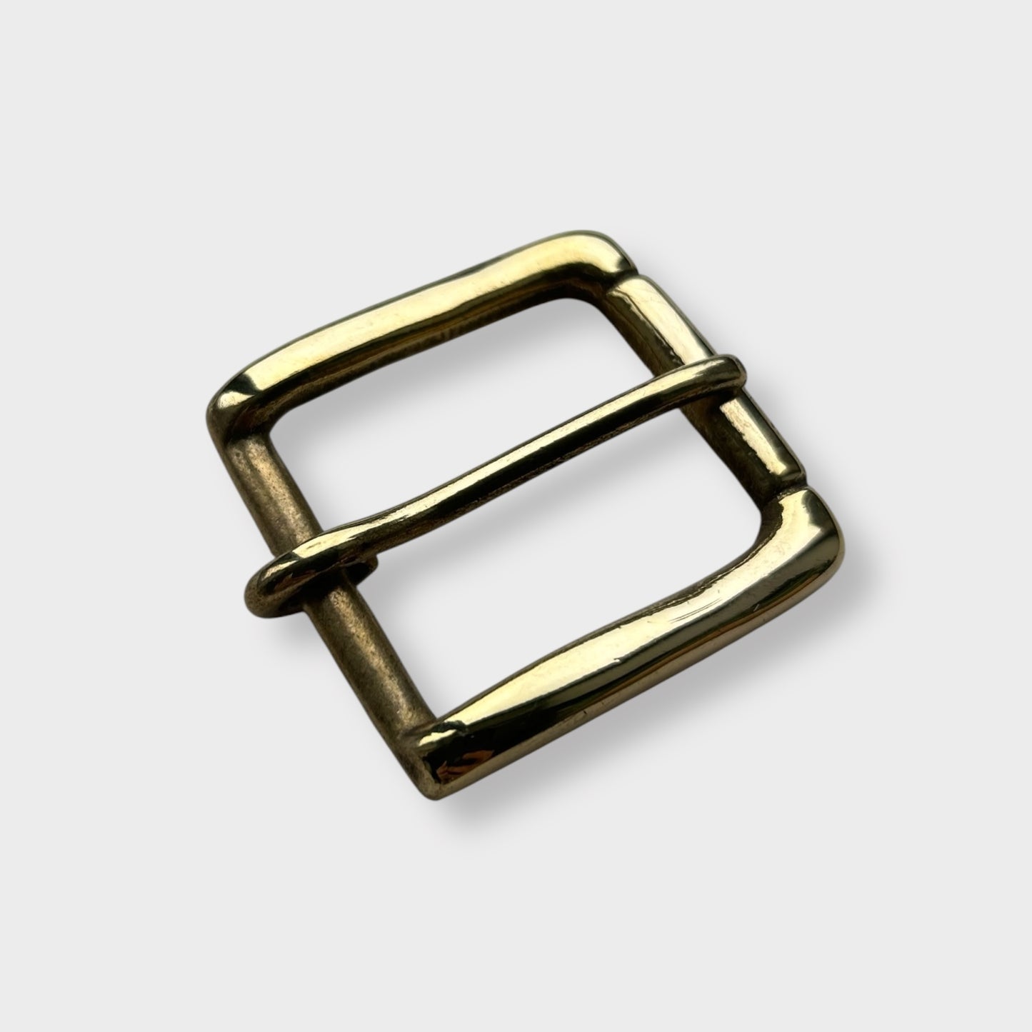 Gold coloured brass metal buckle on a light grey background.