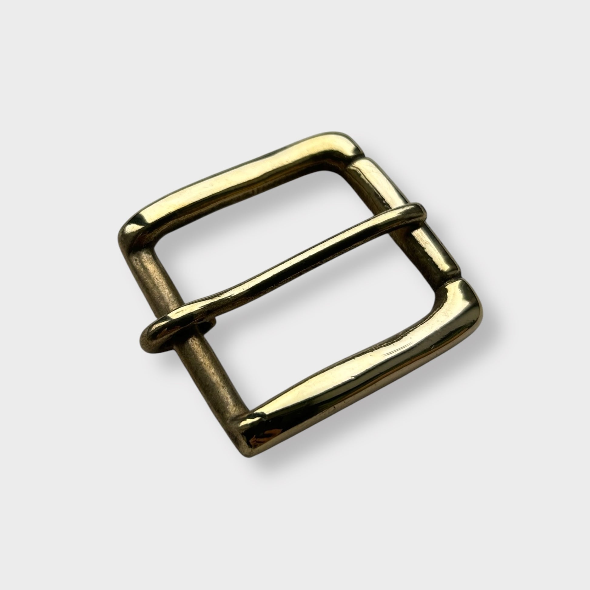 Gold coloured brass metal buckle on a light grey background.
