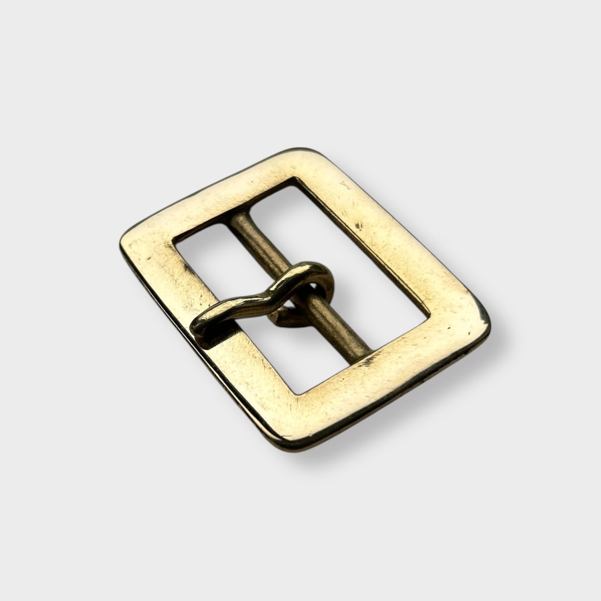 Gold coloured brass metal buckle on a light grey background.
