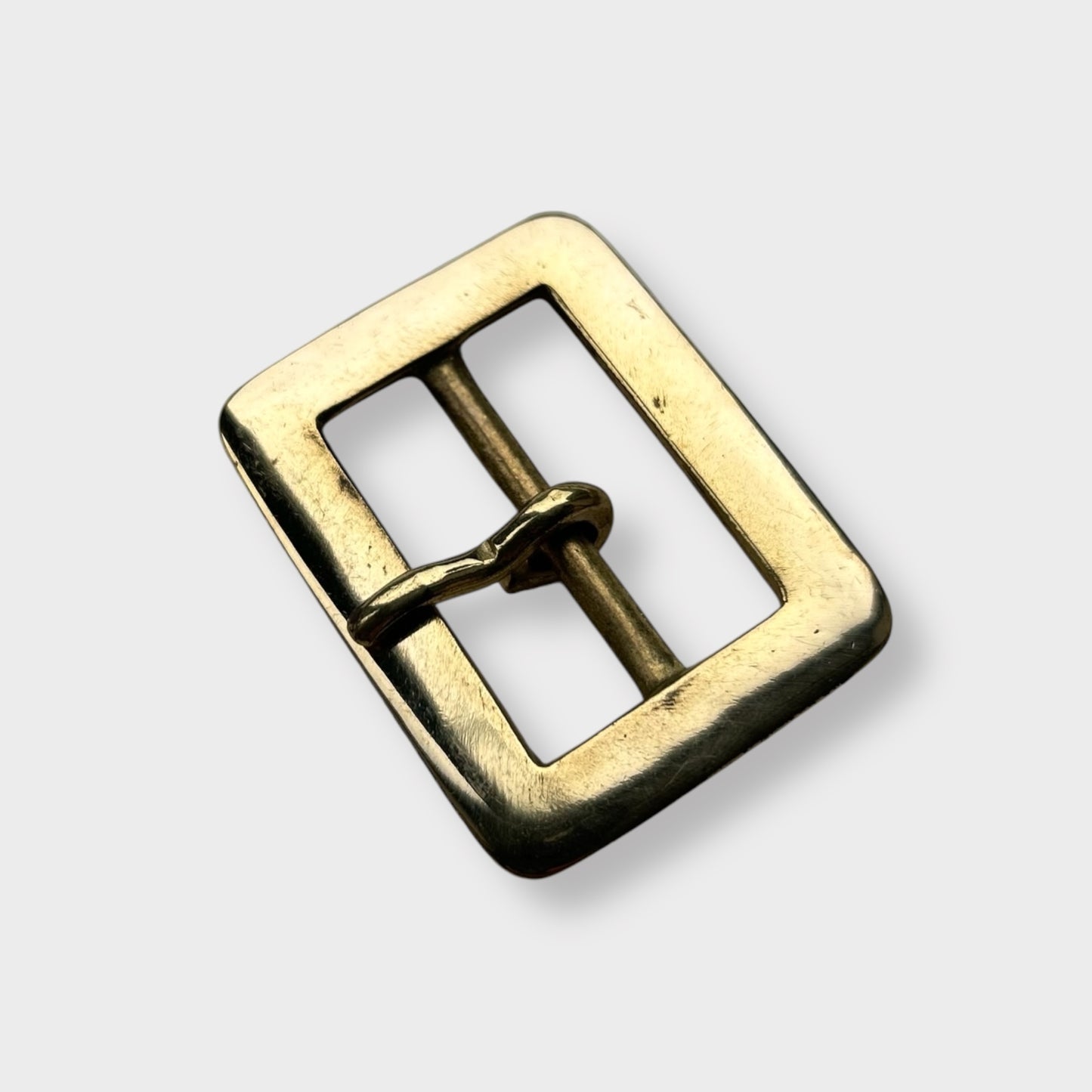 Gold coloured brass metal buckle on a light grey background.