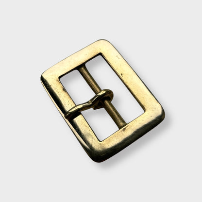 Gold coloured brass metal buckle on a light grey background.