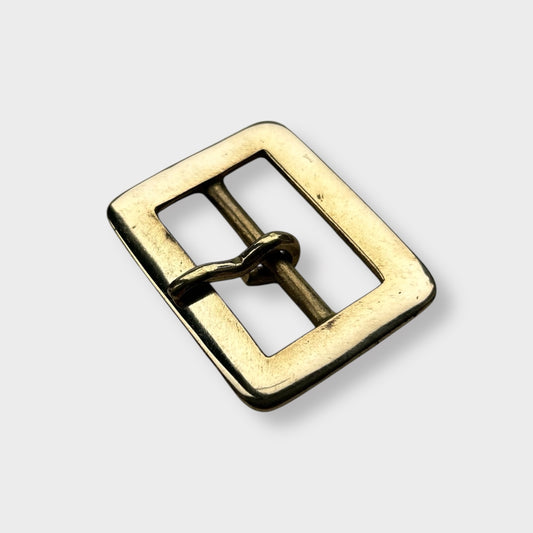 Gold coloured brass metal buckle on a light grey background.