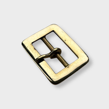 Gold coloured brass metal buckle on a light grey background.