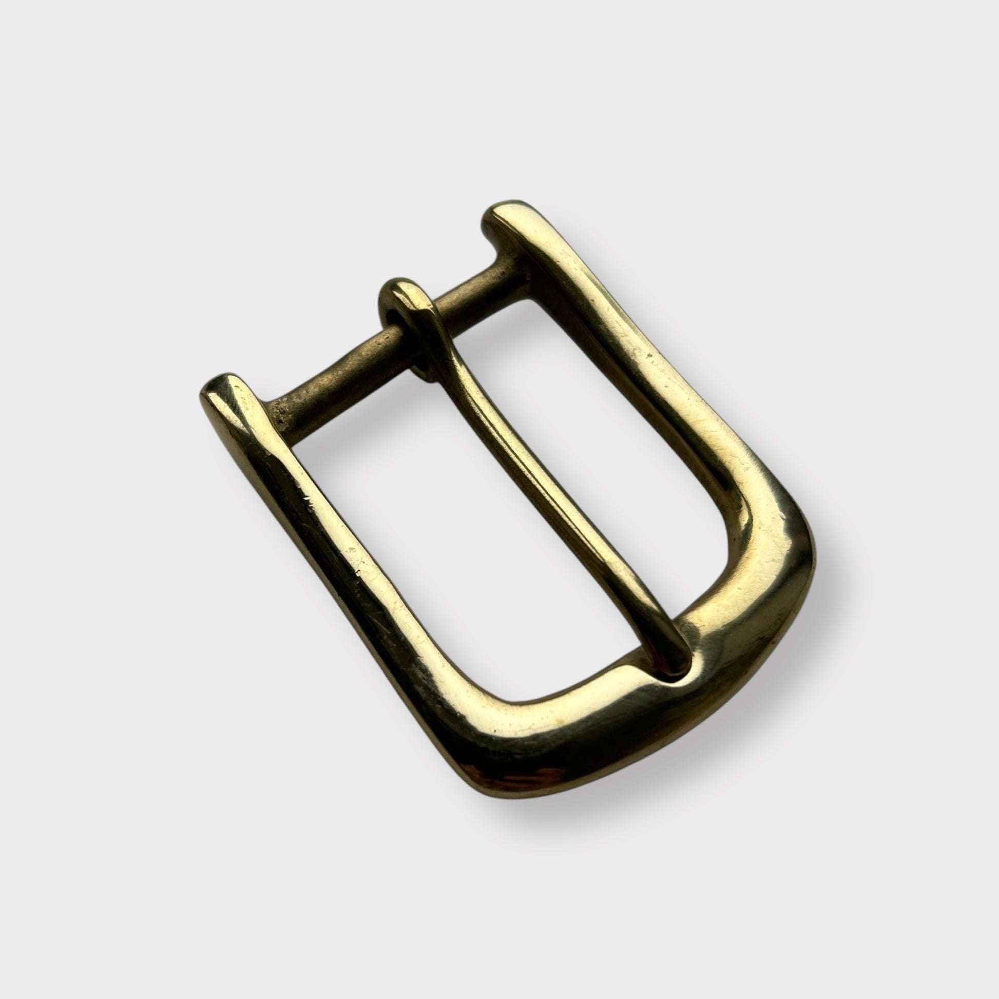 Gold coloured brass metal buckle on a light grey background.