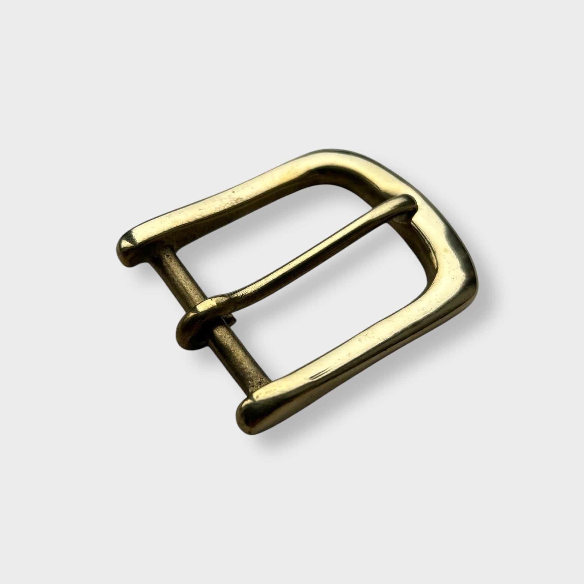 Gold coloured brass metal buckle on a light grey background.