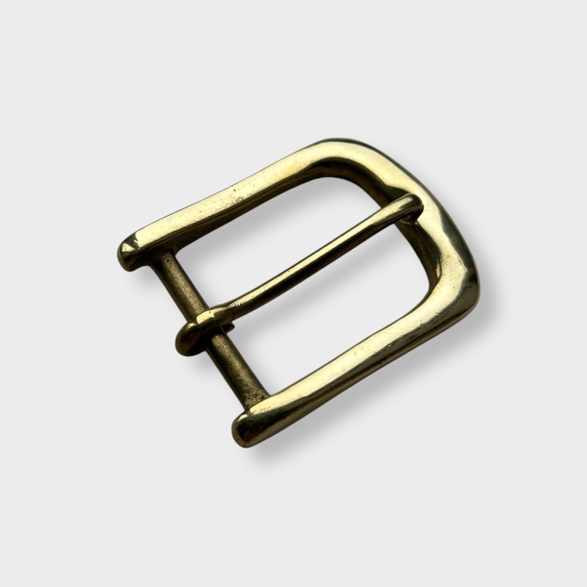 Gold coloured brass metal buckle on a light grey background.