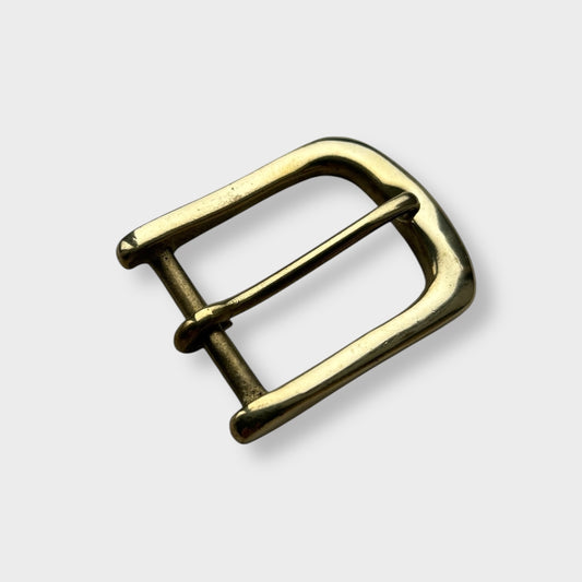 Gold coloured brass metal buckle on a light grey background.