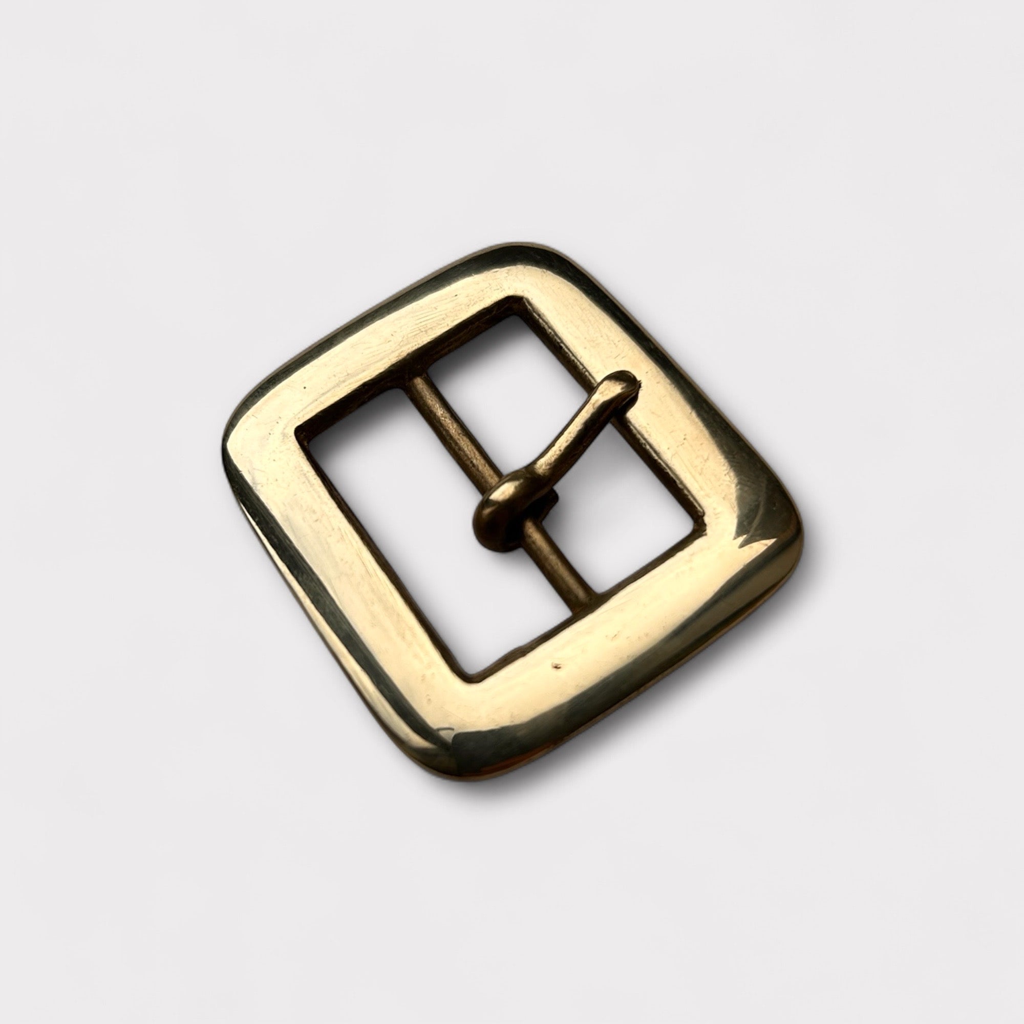 Gold coloured brass metal centre bar buckle on a light grey background.