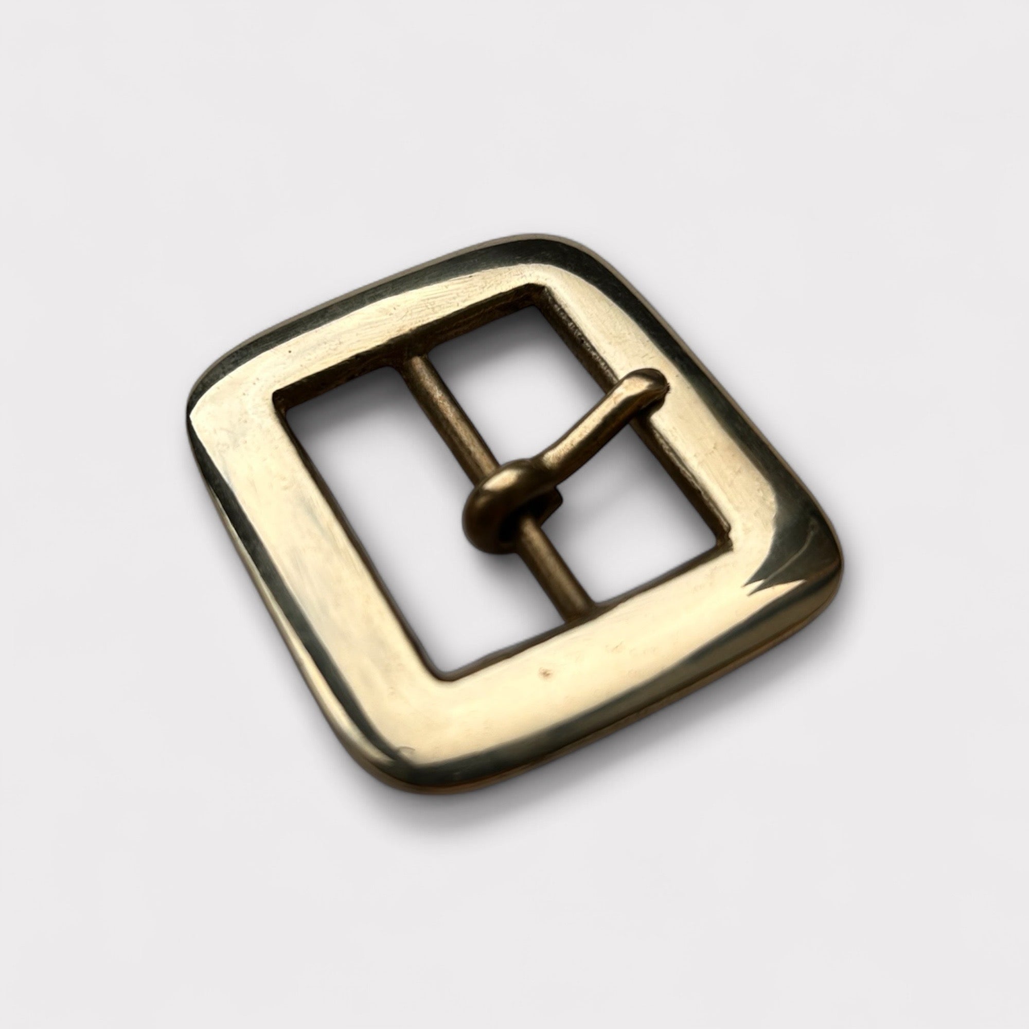 Gold coloured brass metal buckle on a light grey background.