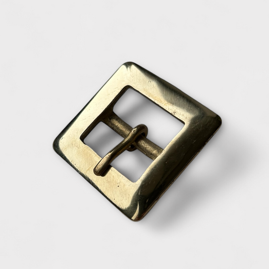 Brass-coloured square metal buckle on a light grey background