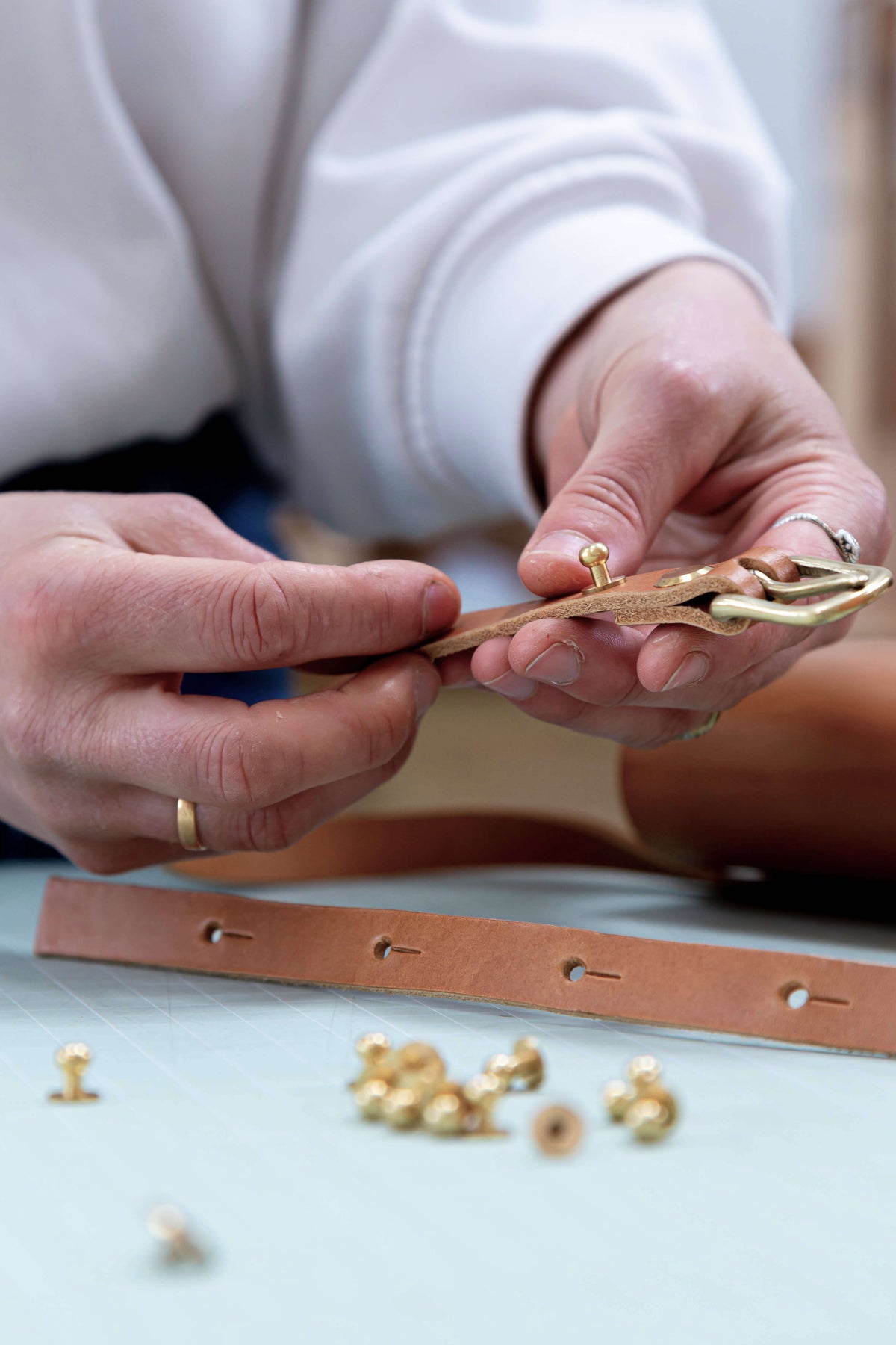 Leather work in progress with hands inserting brass leather hardware into a bag